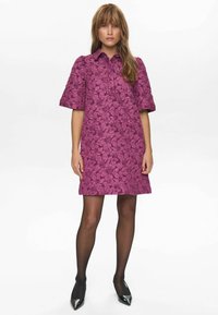 Rochie cu mâneci scurte dintr-un material texturat de culoare purpurie, cu un model floral, având un guler și o siluetă dreaptă, asortată cu ciorapi negri.