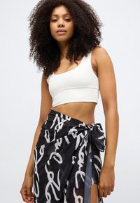 Top corto bianco abbinato a una gonna avvolgente nera con un motivo e design grigi ondulati e dettaglio a nodo laterale. Tessuto liscio, silhouette aderente.