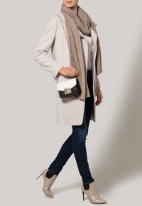 Cappotto beige chiaro, sciarpa grigia, top bianco, jeans scuri e stivaletti con tacco color nudo. Piccola borsa a mano bianca e nera con dettagli in metallo.
