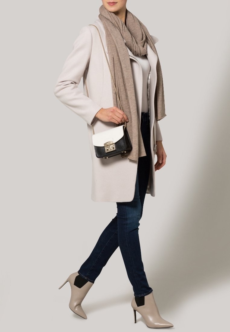 Cappotto beige chiaro, sciarpa grigia, top bianco, jeans scuri e stivaletti con tacco color nudo. Piccola borsa a mano bianca e nera con dettagli in metallo.