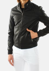 Giacca bomber in pelle nera con zip frontale, polsini a costine e due tasche laterali. La texture liscia e il design aderente accentuano la silhouette.