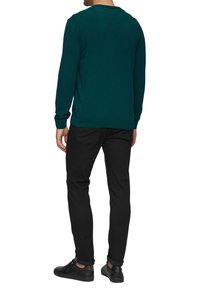 Türkiser Strickpullover mit rundem Halsausschnitt, kombiniert mit schwarzen Slim-Fit-Hosen und schwarzen Sneakers. Der Pullover hat gerippte Bündchen und einen gerippten Saum.