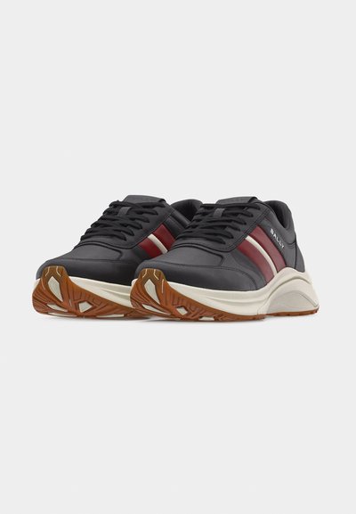 Baskets en cuir noir avec des bandes latérales rouge foncé et blanches, semelles intermédiaires blanches et semelles extérieures texturées marron, présentées en angle pour montrer les détails avant et latéraux.