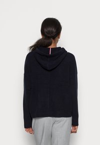 Námořnická mikina s kapucí z měkké látky s uvolněným střihem, která má kontrastní pruhovaný detail kolem krku. Jednoduchý design na zadní straně.