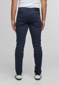 Námořnické modré kalhoty slim fit, vyrobené z elastického bavlněného směsi. Mají zadní kapsy s klopami a nášivku s logem na pasu.