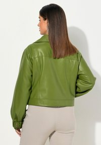 Veste cropped en simili cuir vert avec un col, des poignets boutonnés et une texture lisse, présentant une coupe ajustée et des détails simples.