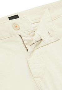 Pantaloni in cotone beige con chiusura a bottone e cerniera, presentano cuciture a contrasto e dettagli discreti delle tasche.