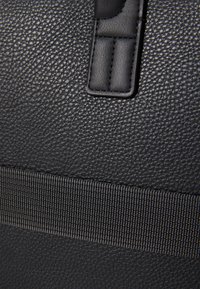 Black textured synthetic material with a matte finish, featuring a wide woven strap and a small padded accent on the side.