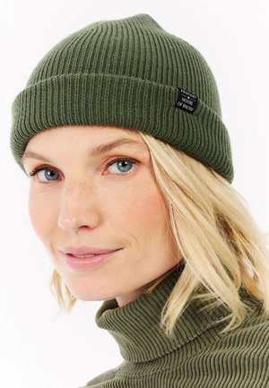 Bonnet en tricot côtelé vert olive avec un revers et une petite étiquette noire sur le côté indiquant "PROTEST HOUSE OF SNOW".