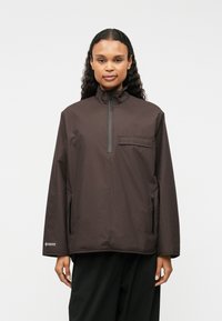 Rjava pulover jakna, visok ovratnik, pol zadrgo spredaj, žep na prsih, dva stranska žepa z zadrgo, lahkotni material, sproščen kroj, minimalističen dizajn.