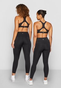 Top cropped atlético preto com design de alças cruzadas, combinado com leggings de cintura alta. Apresenta tecido elegante e detalhes minimalistas.