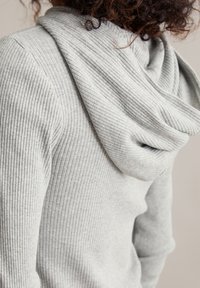 Grijze geribbelde hoodie met een gedrapeerde kraag. Zachte textuur en aansluitende pasvorm, met lange mouwen en subtiele stikdetails.
