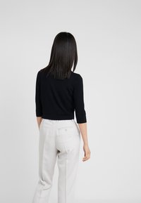 Schwarzes kurzes Top mit Dreiviertelärmeln, kombiniert mit hellbeigen Hosen mit einer Gesäßtasche und einem Knopf. Schlichtes und elegantes Design.