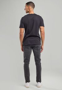 Black cotton t-shirt with short sleeves, paired with dark grey denim jeans. Sneakers are white, with textured detailing on the soles.