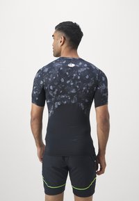 Musta ja tumehall lühikeste varrukatega sporttop, millel on kamuflaažimuster, sobituv disain ning logo detail taga.