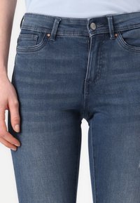 Vaqueros de mezclilla azul oscuro con un diseño ajustado, que cuentan con cinco bolsillos, una cintura con cinturilla y un cierre frontal con botón.