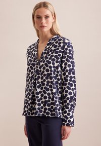 Blusa a pois blu navy e bianca con maniche lunghe, scollatura a V e vestibilità rilassata. Tessuto liscio con dimensioni dei pois variabili, orlo ben cucito.