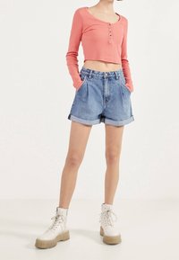 Pink ribbed long-sleeve top with button detail and cropped design, paired with high-waisted denim shorts and chunky white lace-up boots.