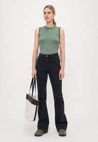 Stripet grønn ermeløs topp, høytlivs svarte jeans, beige totebag med svarte detaljer, og olivengrønne joggesko. Enkelt design.