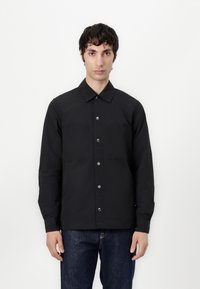 Svart skjorte med knapper, som har krage, to brystlommer, sølvknapper og teksturert stoff, kombinert med mørke denim.