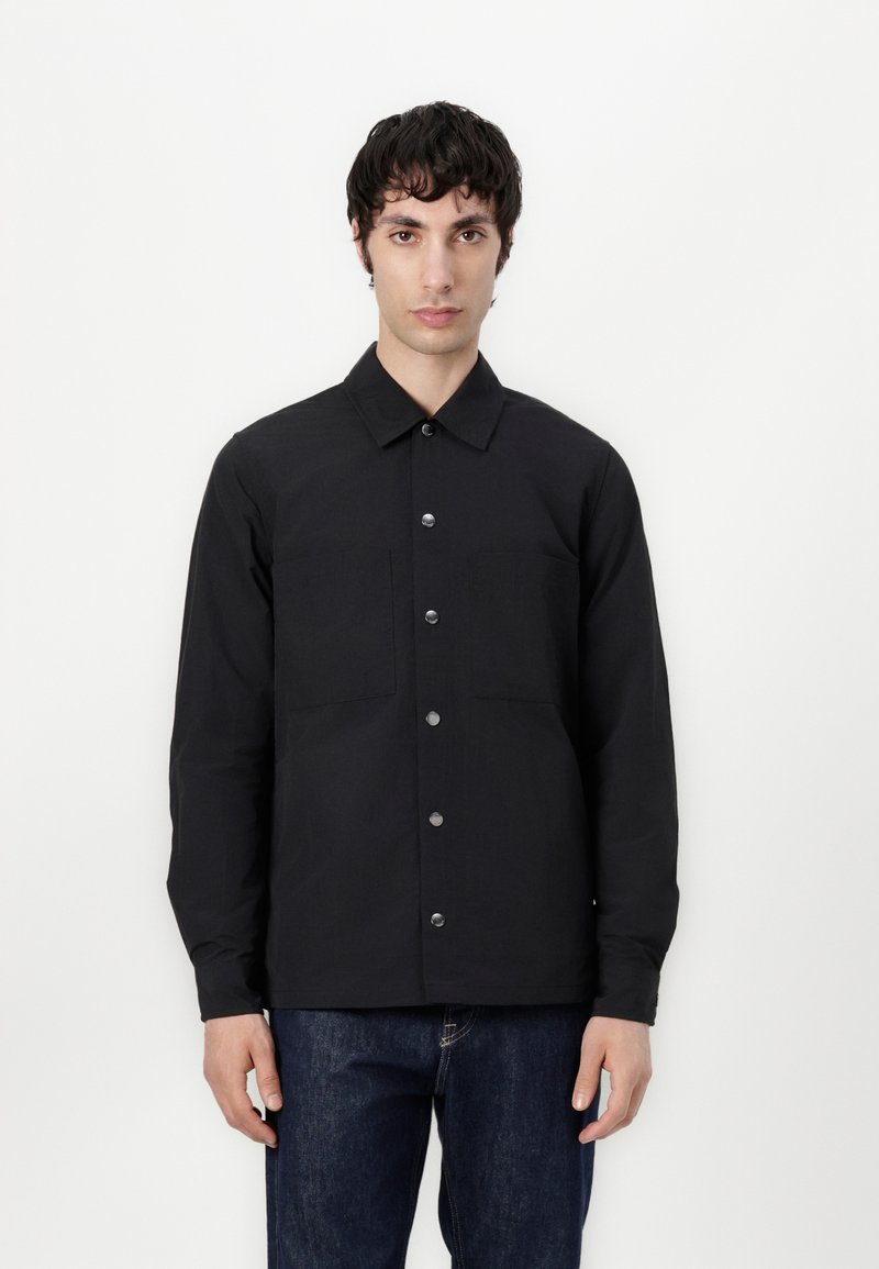 Svart skjorte med knapper, som har krage, to brystlommer, sølvknapper og teksturert stoff, kombinert med mørke denim.