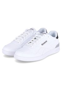Zapatillas blancas Reebok con parte superior de cuero liso, cierre de cordones, puntera perforada, detalles en gris y negro en el talón, y suela de goma blanca.