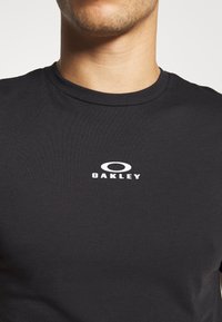 Sort kortærmet T-shirt lavet af bomuld, med en rund hals og et hvidt "Oakley" logo på brystet. Glat tekstur, tætsiddende design.