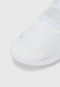 Baskets blanches avec dessus en maille texturée, semelle en caoutchouc lisse et logo Nike gris. Dotées d'une sangle élastique au milieu du pied.