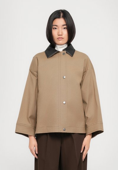 Chaqueta marrón de gran tamaño con un cuello negro, botones a presión y mangas anchas. Tejido suave con detalles de costura mínimos.