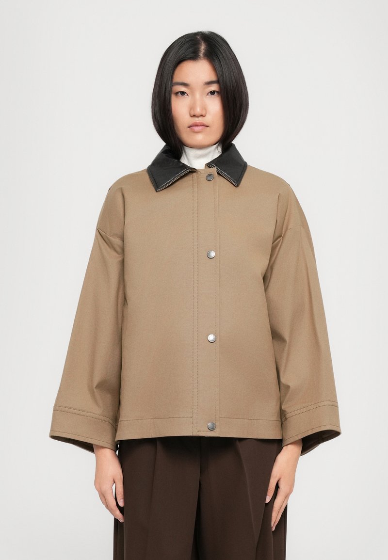 Veste oversized marron avec un col noir, des boutons-pression et des manches larges. Tissu lisse avec des détails de couture minimaux.