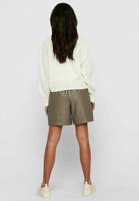 Witte gebreide trui met lange mouwen, gecombineerd met olijfgroene leren shorts. Model in lichte sneakers, gezien vanuit de achterkant.
