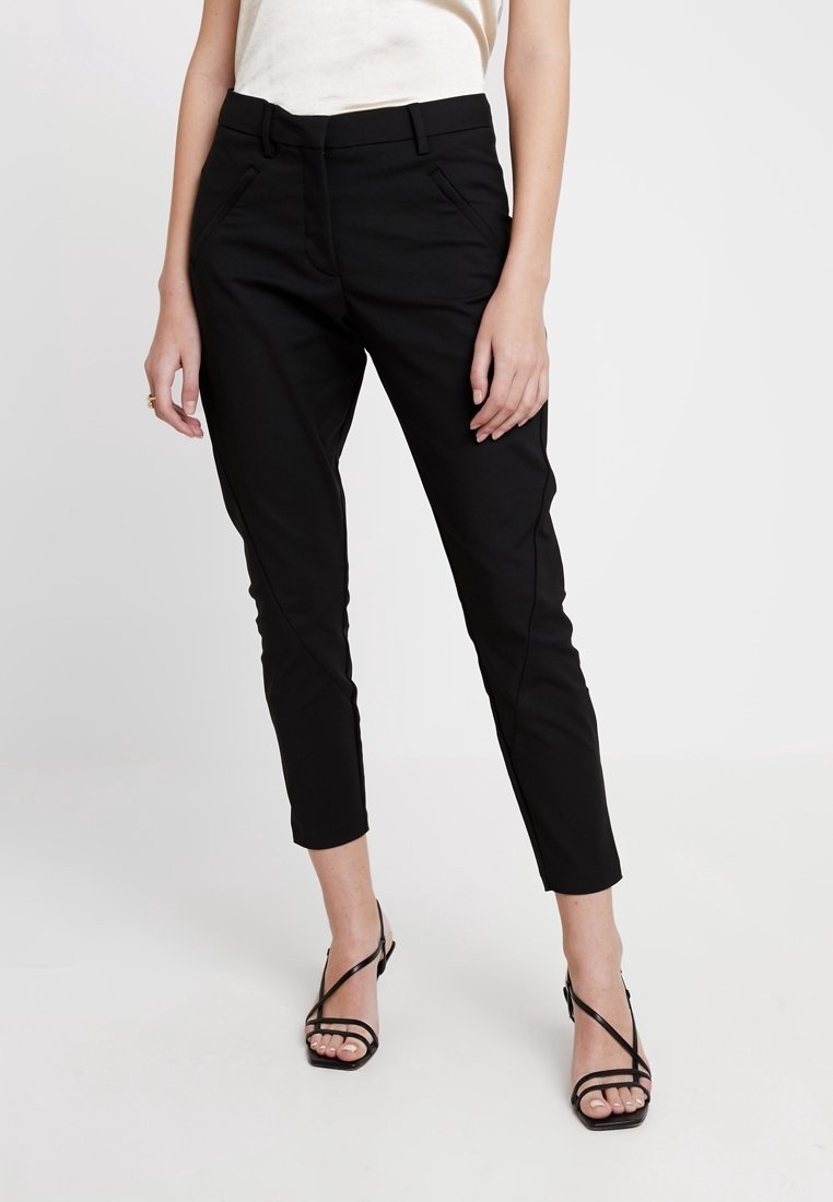 Černé kalhoty s úzkým střihem, které mají přední kapsy a hladkou textura. Akcentovány jemným prošitým pruhem podél nohavic.
