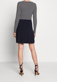 Haut à rayures à manches longues associé à une robe marine, en tissu doux, avec un ourlet évasé et des talons à lanières noirs. Les chaussures présentent un design à lacets et des talons stilettos.