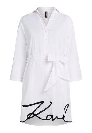 Λευκό βαμβακερό φόρεμα με κολάρο, κουμπιά μπροστά και μακριά μανίκια. Διαθέτει ζωνάκι που δένει στη μέση και μαύρη διακοσμητική λεπτομέρεια με την υπογραφή "Karl".
