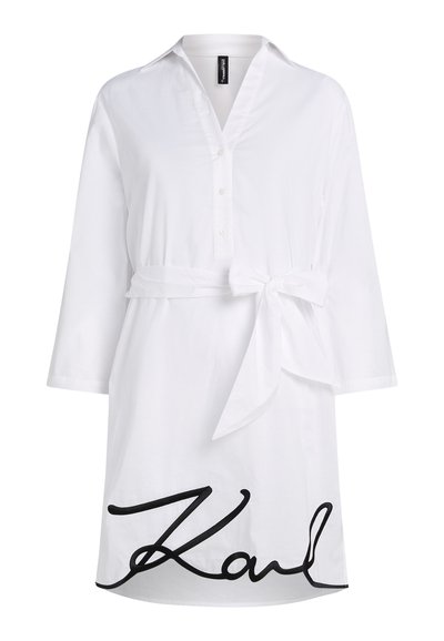 Robe-chemise blanche à manches longues avec col, ouverture boutonnée à l’avant, nœud à la taille et grand texte manuscrit noir près de l’ourlet indiquant "Karl".