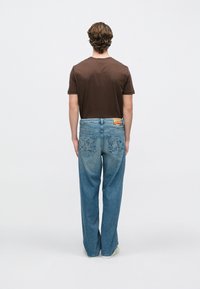 Tricou maro și blugi din denim bleu deschis. Blugii au cusături complexe pe buzunarele din spate. Croială simplă, confortabilă, cu un finisaj decolorat.