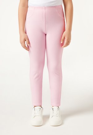 Rosa dehnbare Leggings mit glatter Textur und schmaler Passform, ausgestattet mit zwei seitlichen Taschen. Getragen mit weißen Sneakern.