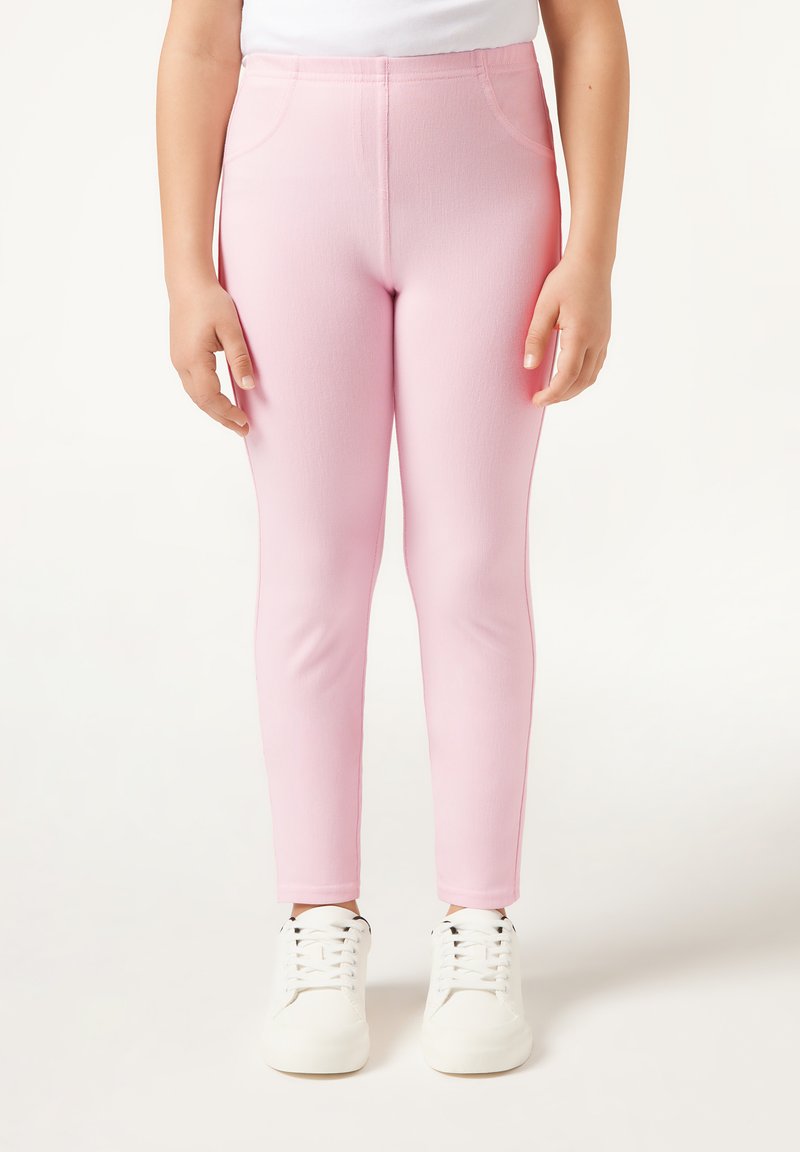 Leggings rosas elásticos con una textura suave y un ajuste ceñido, que cuentan con dos bolsillos laterales. Usados con zapatillas blancas.