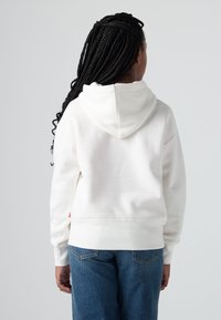 Felpa bianca con cappuccio, dal texture morbido, spalle scese e polsini a costine. Abbinata a jeans di denim blu. Etichetta visibile di lato.