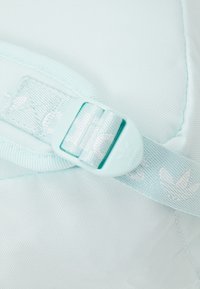 Ljust blå justerbar rem med Adidas-logotyp tryckt på nylonmaterial och en matchande plastspänne på ryggsäcksmaterial.