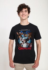 Černé tričko s barevným grafikou "Gremlins" zobrazující více postav a text, s kulatým výstřihem, krátkými rukávy a z bavlněné tkaniny.
