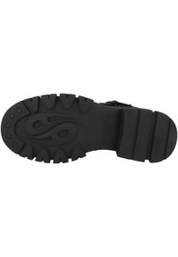 Suela de bota de goma negra con superficie texturizada, surcos profundos y un diseño de logo prominente. Patrón de agarre fuerte para tracción y durabilidad.