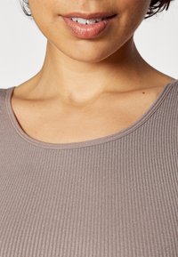Short-sleeve, ribbed top in a soft, muted mauve color with a rounded neckline and a smooth, textured finish. Subtle shine in fabric.