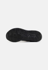 Black rubber shoe sole with textured treads and grip patterns, featuring deep grooves and a rounded toe design for traction.