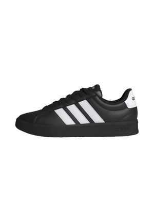 Zapatilla Adidas negra con rayas blancas, suela negra, diseño con cordones y lengüeta blanca en el talón con el logo de Adidas, mostrada de perfil.