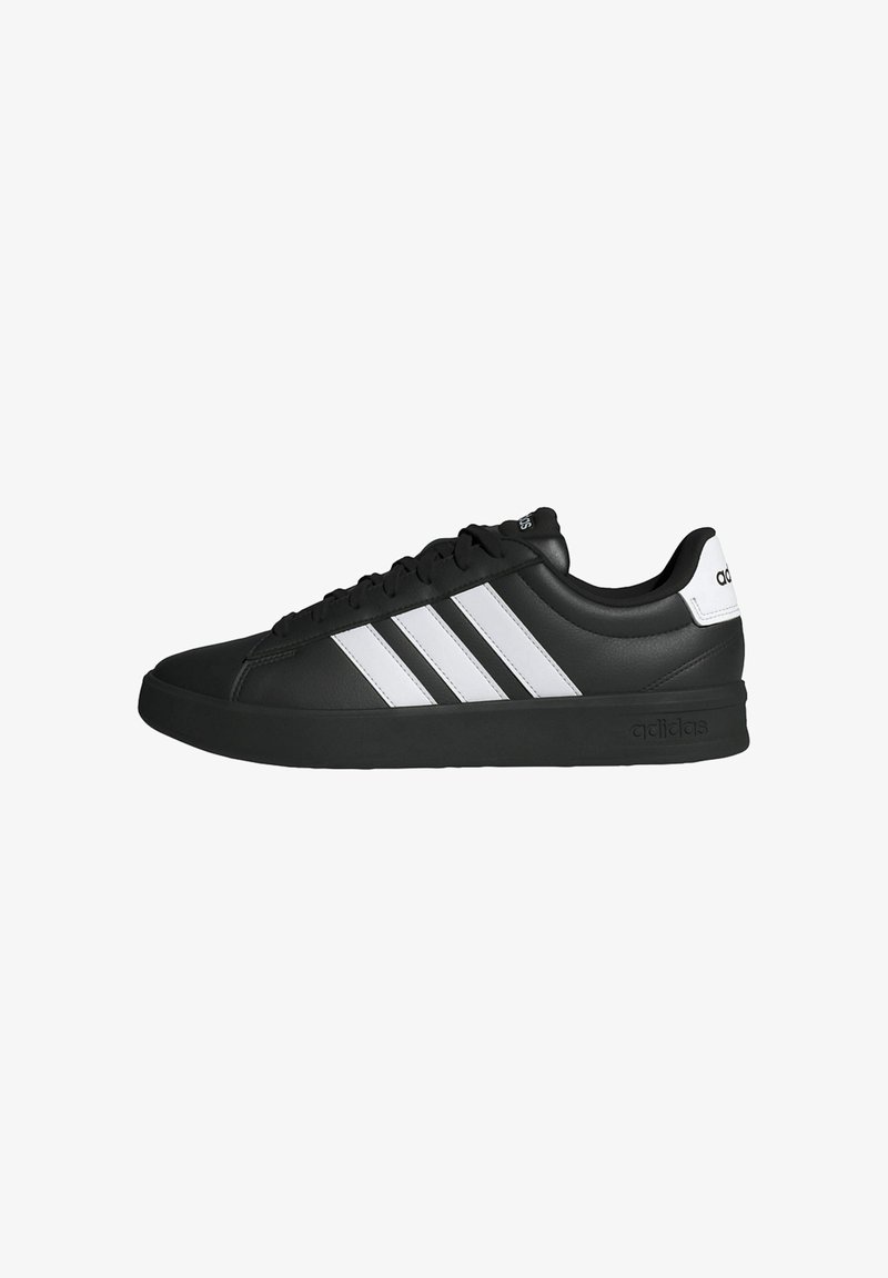 Basket Adidas noire avec bandes blanches, semelle noire, design à lacets et languette blanche au talon avec le logo Adidas, vue de profil.