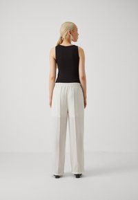 Bodysuit sans manches noir associé à un pantalon large écru. Le pantalon présente un tissu texturé et une taille élastique.