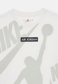 Hvit T-skjorte med en stor grå Nike-logo og et svart "AIR JORDAN"-merke. Inkluderer en silhuett av en basketballspiller i aksjon.