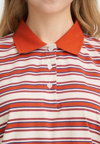 Polo à col avec des rayures horizontales rouges, bleues et blanches. Confectionné en tissu doux, il comporte trois boutons blancs sur le devant.