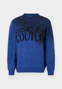 Kék kötött pulóver kerek nyakkal és bordás mandzsettával. Az elején a "VERSACE JEANS COUTURE" felirat látható feketében.